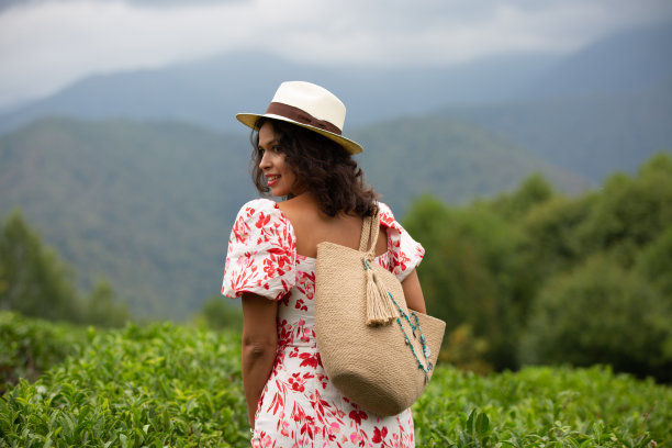 这张照片是一个混血女孩的背影，她戴着草帽，穿着一件衣服，肩上背着一个草包，走在一个茶园的中央图片下载