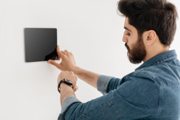 阿拉伯男人使用墙上的恒温器智能家居控制面板调节室温图片下载