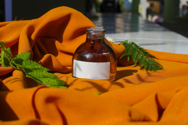 香水瓶与空白白色标签和绿色叶子在纹理的橙色织物背景。香水瓶库存照片图片下载