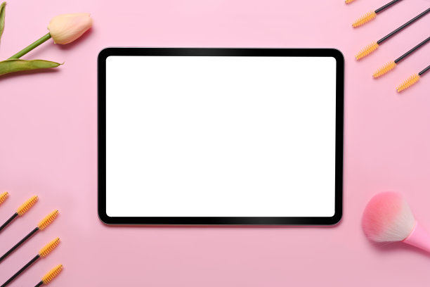 粉色背景上的数码平板电脑和化妆刷。图片下载