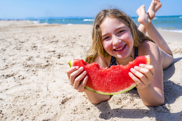 女孩在白沙上吃西瓜图片下载