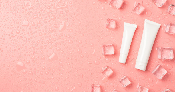 俯视图照片的白色奶油瓶和balm管没有标签的冰块在右边和滴在孤立的淡粉色背景与copyspace在左边图片下载