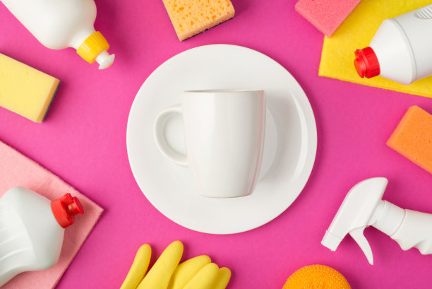 俯视图照片白色干净的杯子在盘子在中间洗涤垫破布橡胶手套和白色洗涤剂瓶孤立的粉红色背景图片下载