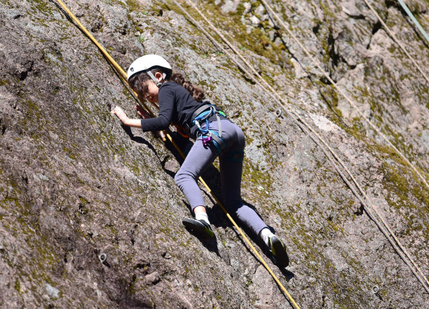 一个年轻的女孩正在攀岩。一个女孩拿着绳子在岩石上从事攀岩运动。图片下载