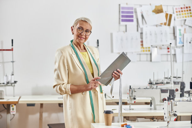肖像快乐的中年妇女时装设计师与时尚的眼镜和卷尺在光车间图片下载