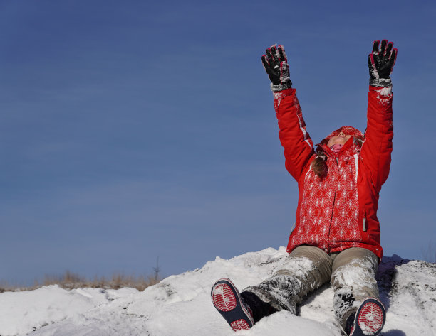 在阳光明媚的日子里，快乐的孩子坐在雪地上，抬起双臂，望着美丽的蓝天。冬季儿童活动理念。图片下载
