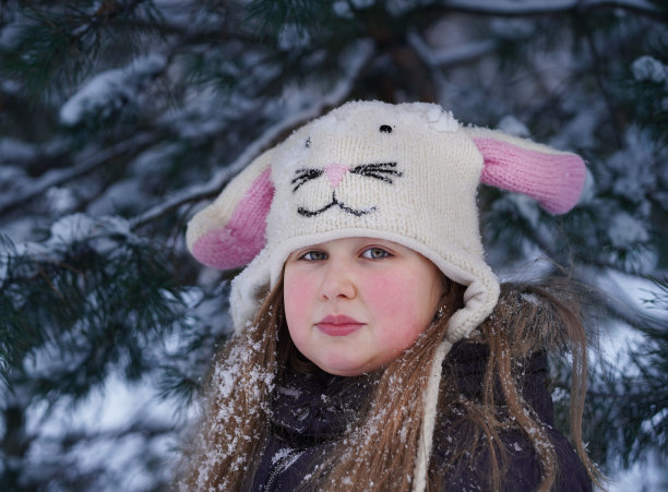 长头发的小女孩戴着滑稽的针织帽和长兔子耳朵在冬天的公园玩得很开心。雪盖住了她的帽子和头发。肖像。看相机。图片下载