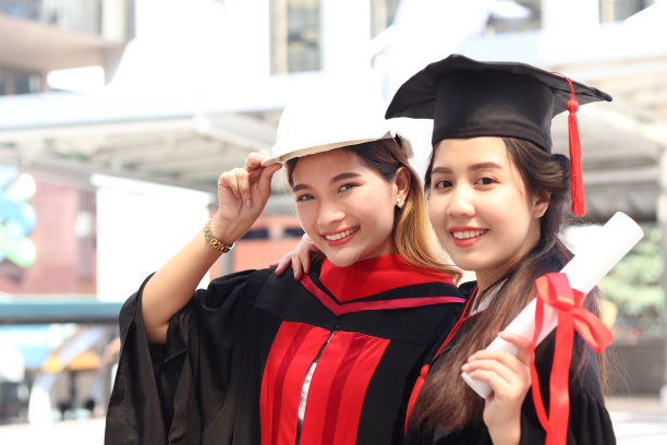 两个快乐微笑的毕业生持有证书的肖像，年轻美丽的亚洲妇女看着相机在他们的毕业典礼上如此自豪，人们庆祝成功的教育毕业日当已经完成大学学习或图片下载