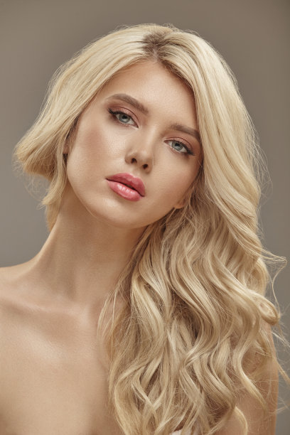 垂直拍摄的漂亮女孩肖像与卷曲的金发和干净的皮肤，工作室的美丽图片上的米色背景图片下载