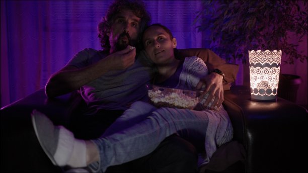 一对夫妇晚上在沙发上看电视吃爆米花。图片下载