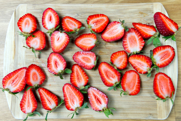 新鲜草莓片和叶子放在桌上的木板上图片下载