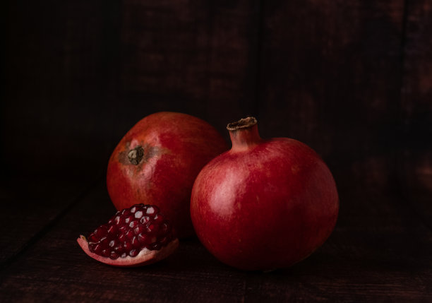 多汁的成熟石榴，暗红色，背景上有一小块破碎的石榴和果粒。图片下载