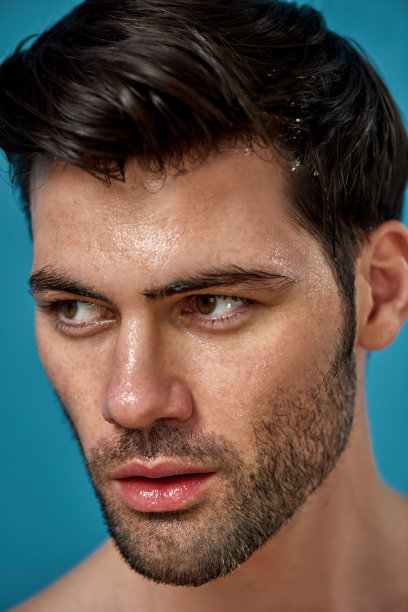 近景肖像英俊的黑发男子与湿洗脸一边看，在蓝色背景孤立图片下载