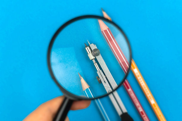 男人拿着放大镜，看着铅笔中间画着指南针，蓝色的桌子背景，几何概念照片图片下载
