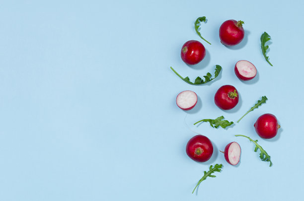 萝卜和芝麻菜阴影在蓝色背景作为边框，俯视图，复制空间。五彩缤纷的春菜背景。图片下载