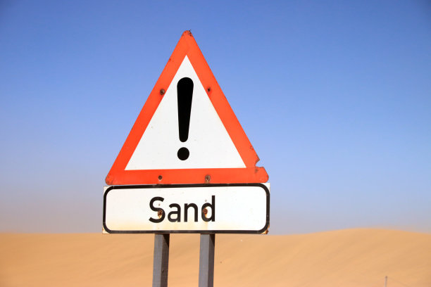 靠近纳米比亚的警告有沙子进入的路标。以沙丘和蓝天为背景的警告标志。图片下载