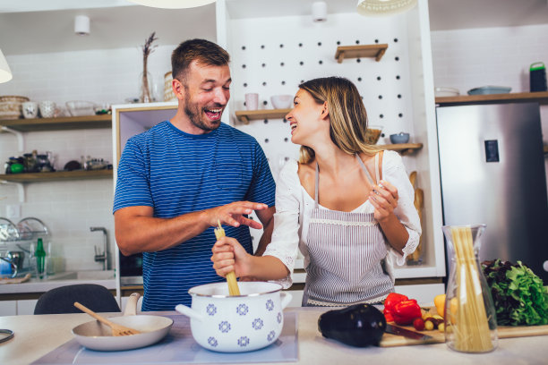 一对美丽的年轻夫妇正在谈笑风生，在厨房里做着健康的食物。图片下载