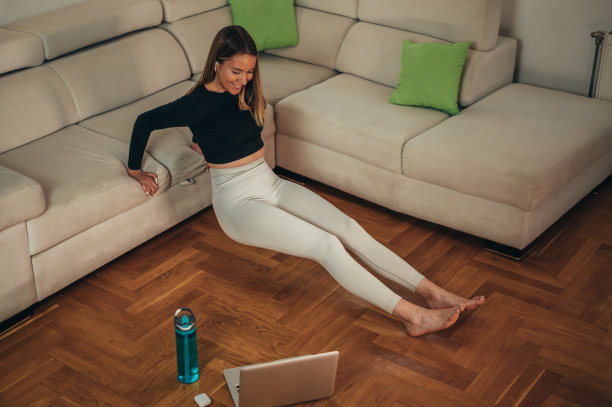 年轻迷人的女人在家里训练，同时使用笔记本电脑图片下载