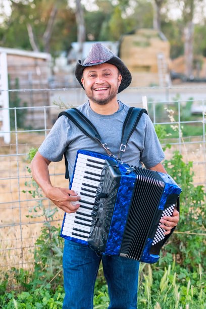 面带微笑的成熟的墨西哥农业工人在一个农场拉手风琴，戴着牛仔帽图片下载