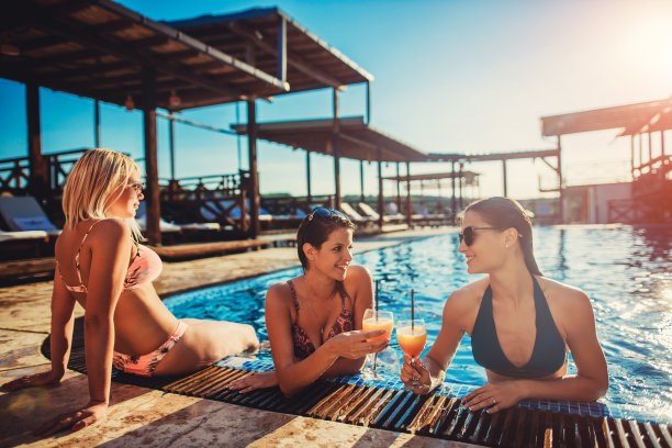 两个女人和一个男人享受在游泳池在一个阳光明媚的夏天库存照片。图片下载