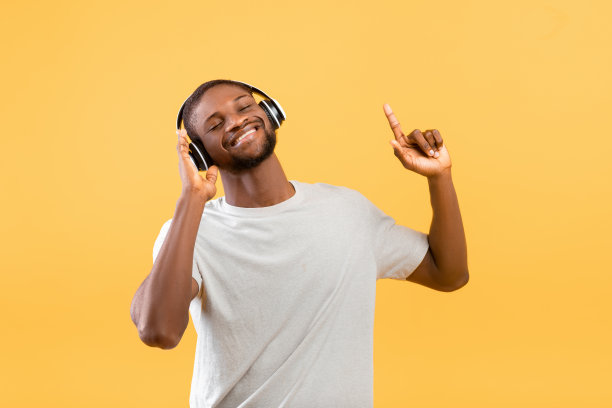 快乐的非裔美国人戴着无线耳机听着音乐，在黄色的录音棚背景上跳舞图片下载