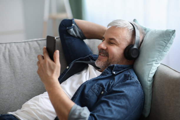 头发花白的男人戴着耳机用智能手机听音乐图片下载
