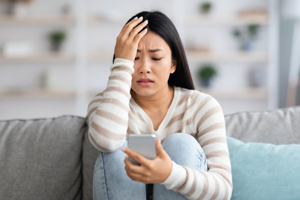 坐在家里沙发上看智能手机屏幕的担忧亚洲女人图片下载