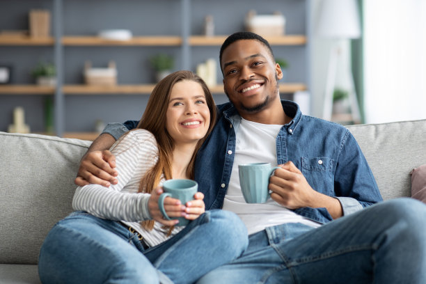 居家休闲：情侣在沙发上看电视喝咖啡图片下载
