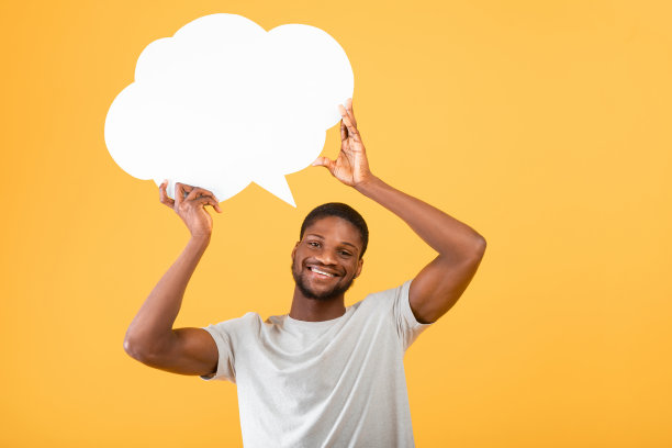 兴奋的非裔美国人举着空的演讲泡在他的头上，在黄色的背景上摆姿势图片下载