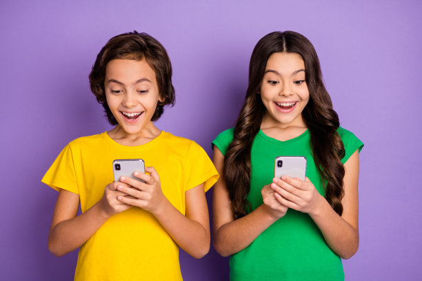 年轻开朗的孩子们的照片快乐的微笑惊奇的惊讶的新闻看阅读浏览手机孤立在紫色的背景图片下载