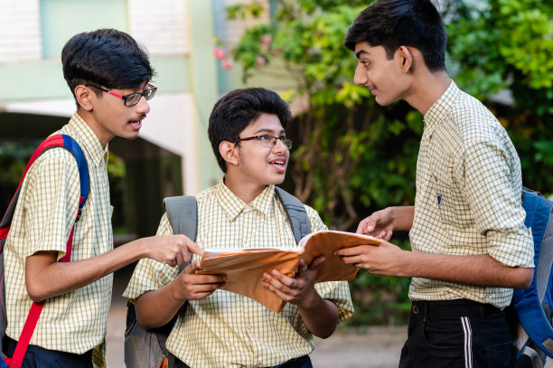 三个年轻的学生在学校大楼外讨论一本书。图片下载
