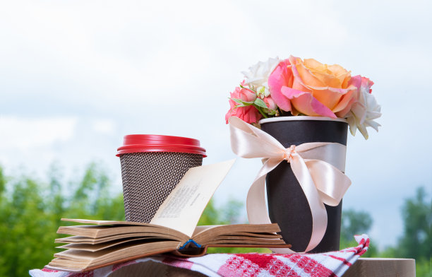 书，玫瑰花和纸杯放在木桌上。蓝色的天空背景。图片下载