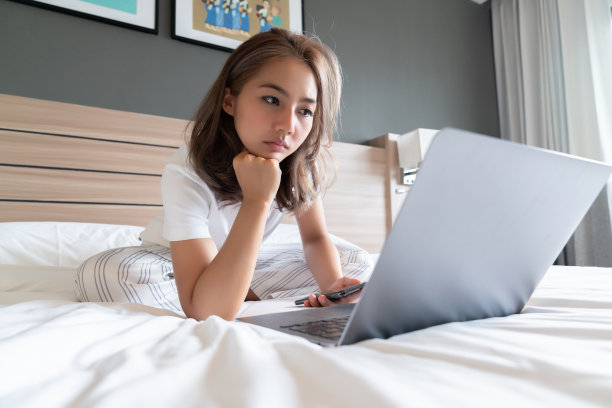 漂亮的亚洲女人躺着微笑着躺在床上和她的笔记本电脑。图片下载