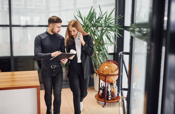 女人和男人穿着正式的衣服拿着文件在办公室里交谈图片下载