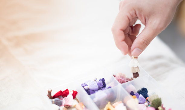 手握多色流苏可选用耳环坠饰或皮包装饰，流苏放在塑料盒上。图片下载