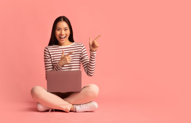 亚洲女人坐在地板上，拿着笔记本电脑，指着复印区图片下载