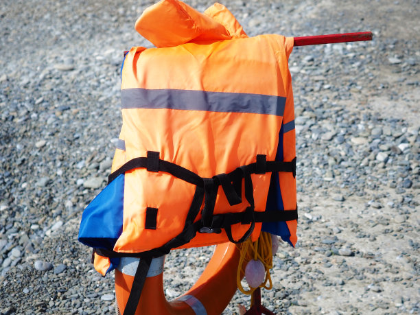 在一个阳光明媚的日子里，一件橙色背心悬挂在卵石滩上的救生圈上图片下载