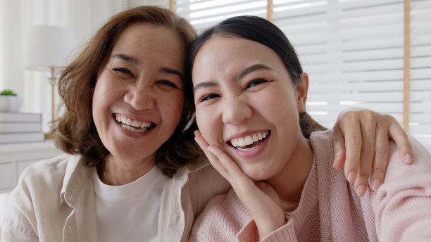 POV迷人美丽的两人亚洲小姐女孩用手机拍照照片视频欣喜若狂地坐在家里沙发沙发一起度过美好的日子隔离在妈妈健康保健。图片下载