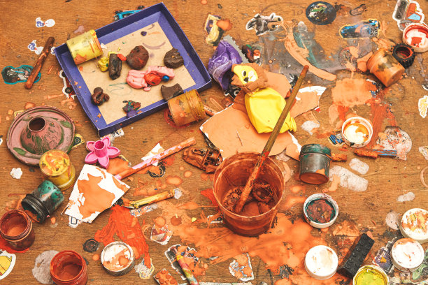 一罐罐的颜料，刷子，橡皮泥和玩具在凌乱的桌子上图片下载