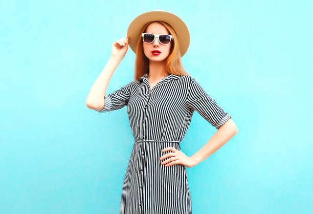 白人年轻女子的肖像戴着夏季草帽，条纹连衣裙上的蓝色背景图片下载