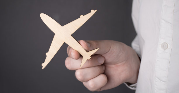 年轻英俊的男子穿着白色衬衫，在灰色背景上拿着一个黄色的飞机模型。孤立的图片下载