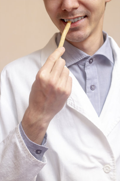一个年轻人穿着白大褂，用一根丝瓦克刷他的牙。亚拉克树，萨尔瓦多桃，圣娜。米色背景。图片下载