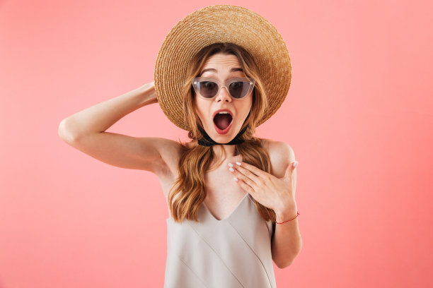 震惊的黑发女人穿着衣服，帽子和太阳镜图片下载