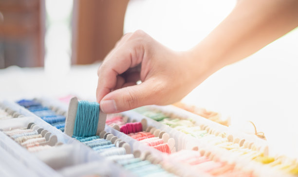 裁缝女士双手合拢，拿着海蓝色的丝线和不同颜色的丝线放在桌子上，准备用白色的棉线和木框搭配使用。图片下载
