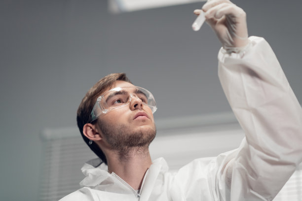 这是一位科学家的特写照片，他举起一个装有液体的试管，对着光仔细观察图片下载