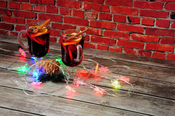 两杯热红酒，一根松枝和松果还有一堆燃烧的圣诞花环放在一张木桌上。图片下载