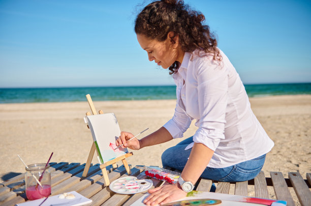 一个美丽的女性画家的侧面肖像在画布上画在海上的露天背景图片下载