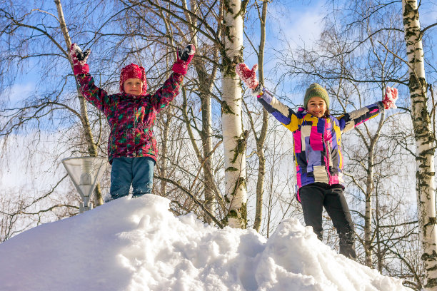 两个有趣的小妹妹正以积极的心情站在雪山上，他们的手向上。图片下载