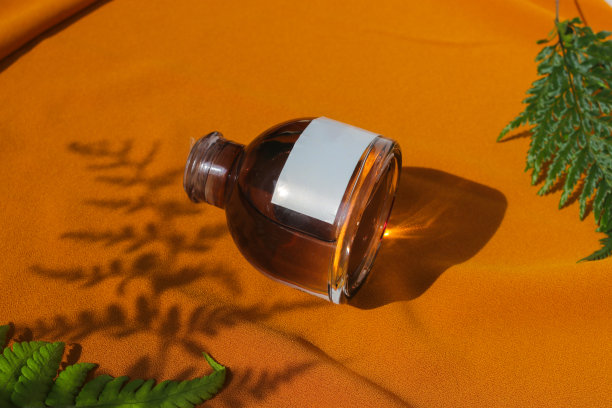 香水瓶与空白白色标签和绿色叶子在纹理的橙色织物背景。香水瓶库存照片图片下载