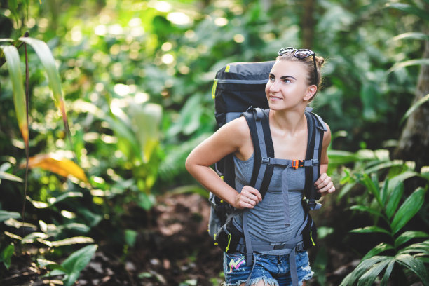 在丛林中背着徒步背包的苗条年轻女孩。一个白人女孩在丛林里徒步旅行。图片下载